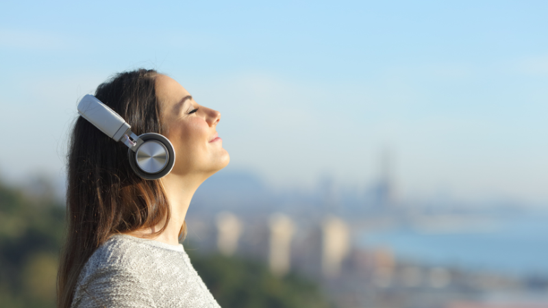 A woman wearing headphones stands outside. Her head is upturned to the sun, her eyes are closed and she has a smile on her face. She's listening to the Sounds of Summer countdown from Walmart Radio!